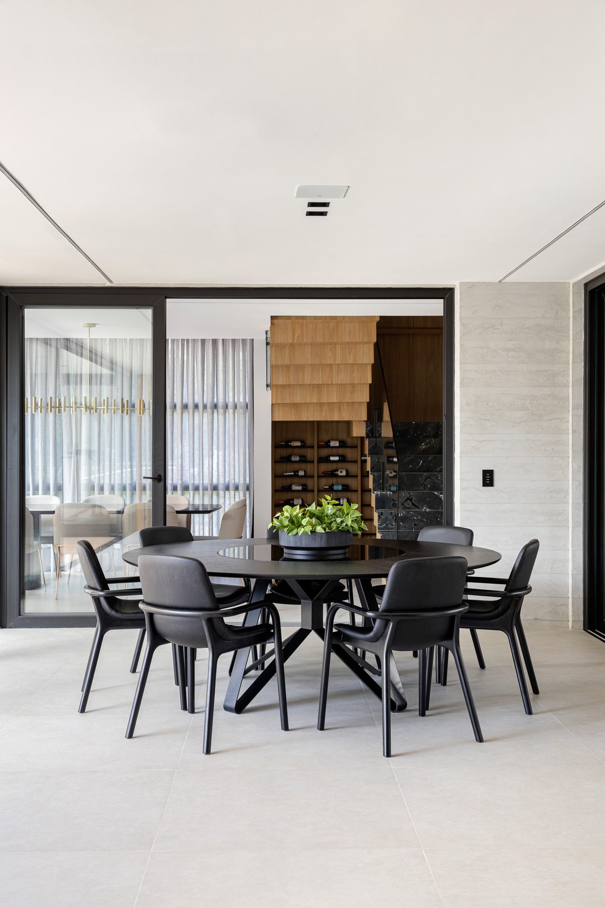 Sala de jantar com mesa redonda preta, cadeiras escuras e vista para o interior da residência